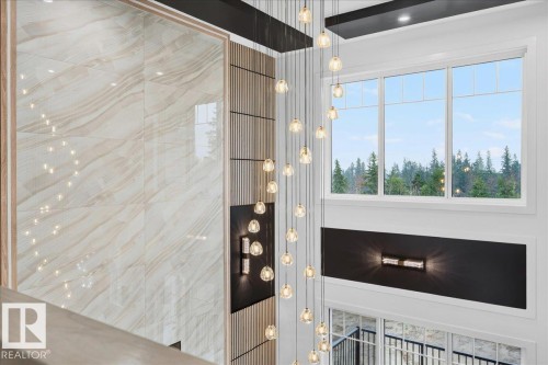 Double-height foyer featuring a multi-tiered chandelier, large picture windows, a decorative accent wall with vertical wood paneling and a light-toned patterned wall finish, and a rectangular wall sconce - 427 172 Avenue Nw, Edmonton, AB - Indoor Photo Showing Other Room