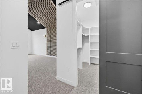 Built-in closet system featuring white shelving and hanging rods, accessible via a barn door - 427 172 Avenue Nw, Edmonton, AB - Indoor