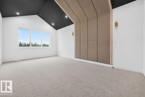 Room featuring a vaulted ceiling with recessed lighting, expansive window, light-toned carpeting, and a slatted wood-finish accent wall with integrated vertical lighting and decorative wall sconces - 427 172 Avenue Nw, Edmonton, AB - Indoor Photo Showing Other Room