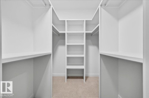 Custom closet system featuring white built-in shelving, multiple hanging rods, and a central shelving unit - 427 172 Avenue Nw, Edmonton, AB - Indoor With Storage