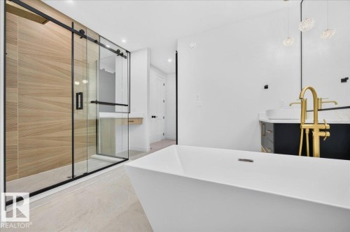 Contemporary bathroom featuring a freestanding soaking tub with a floor-mounted gold-tone faucet, a glass-enclosed shower with wood-look tile, and dual vanities with vessel sinks - 427 172 Avenue Nw, Edmonton, AB - Indoor Photo Showing Bathroom