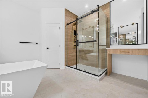Modern bathroom featuring a freestanding soaking tub, a glass-enclosed shower with a black frame and sliding door, light-toned tile flooring, a wall-mounted vanity with a mirror, and a wood-finish accent wall - 427 172 Avenue Nw, Edmonton, AB - Indoor Photo Showing Other Room