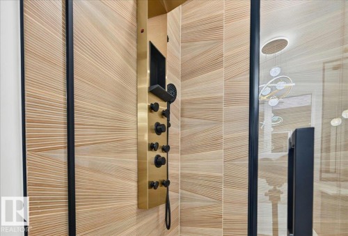 Shower enclosure with wood-finish tiled walls, a brushed gold shower panel with matte black controls, and a clear glass door with a black frame and handle - 427 172 Avenue Nw, Edmonton, AB - Indoor Photo Showing Bathroom