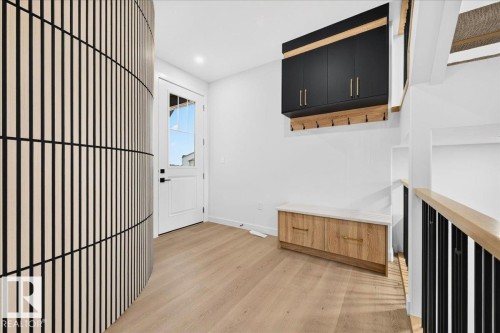 Entryway featuring a unique curved slatted accent wall, light wood-finish flooring, a white glass-paneled door, built-in storage bench with a light-toned countertop, and a wall-mounted black cabinet unit with gold-toned hardware - 427 172 Avenue Nw, Edmonton, AB - Indoor Photo Showing Other Room