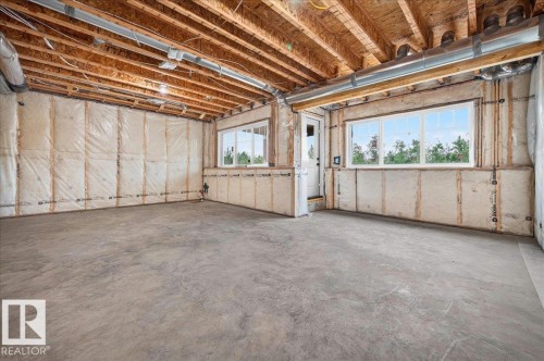 Unfinished lower level featuring exposed wood joists, concrete flooring, two windows, and an exterior door - 427 172 Avenue Nw, Edmonton, AB - Indoor Photo Showing Basement