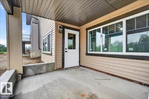 Covered patio area featuring a concrete slab, contrasting dark trim, and a white entry door with an exterior light fixture - 427 172 Avenue Nw, Edmonton, AB - Outdoor With Exterior