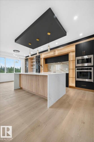 Contemporary kitchen featuring a large central island with waterfall countertop, integrated sink, and wood-finish cabinetry - 427 172 Avenue Nw, Edmonton, AB - Indoor Photo Showing Kitchen