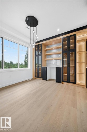 Built-in cabinetry featuring light wood-finish shelving, black-framed glass doors, and integrated lighting - 427 172 Avenue Nw, Edmonton, AB - Indoor