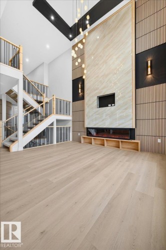 Two-story living area featuring a prominent fireplace wall with integrated media space, a multi-tiered staircase with black metal balusters, and light wood-finish flooring - 427 172 Avenue Nw, Edmonton, AB - Indoor Photo Showing Other Room
