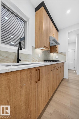 Contemporary kitchen featuring wood-finish cabinetry, white countertops, and a stone-patterned backsplash - 427 172 Avenue Nw, Edmonton, AB - Indoor Photo Showing Kitchen