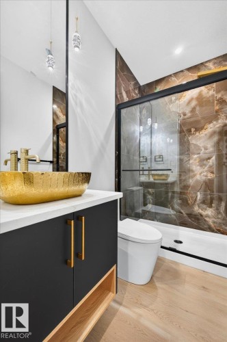 Modern bathroom featuring a black vanity with a white countertop and gold hardware, a gold vessel sink, and a walk-in shower with brown veined tile - 427 172 Avenue Nw, Edmonton, AB - Indoor Photo Showing Bathroom