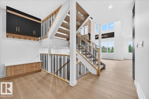 Open-concept entryway featuring wood-finish flooring, a contemporary staircase with black spindles and wood handrails, built-in mudroom cabinetry with black uppers and wood lowers, a built-in bench with a light-toned countertop, and multiple large windows - 427 172 Avenue Nw, Edmonton, AB - Indoor Photo Showing Other Room