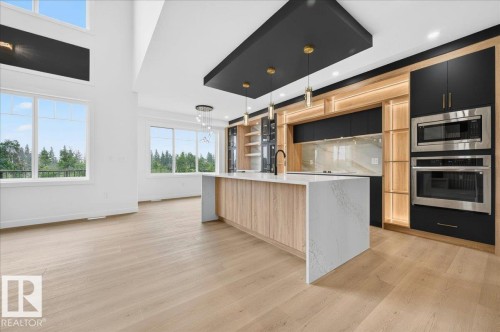 Gourmet kitchen and living area featuring high ceilings, wood-finish flooring, a waterfall island with a quartz countertop, built-in stainless steel appliances, and custom cabinetry with integrated lighting - 427 172 Avenue Nw, Edmonton, AB - Indoor Photo Showing Kitchen