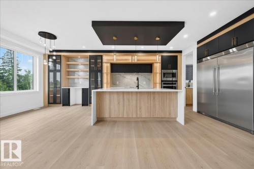 Spacious kitchen featuring a large central island with a waterfall countertop, integrated stainless steel appliances, extensive wood-finish cabinetry, and light wood-finish flooring - 427 172 Avenue Nw, Edmonton, AB - Indoor Photo Showing Kitchen