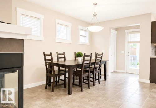 Dining area featuring tile flooring, a contemporary chandelier, multiple windows with blinds, a white door providing exterior access, and a built-in fireplace with a glass front - 5135 1A Avenue Sw, Edmonton, AB - Indoor Photo Showing Dining Room