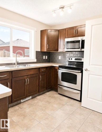 Kitchen featuring wood-finish cabinetry, stainless steel appliances, a subway tile backsplash, and light-toned tile flooring - 5135 1A Avenue Sw, Edmonton, AB - Indoor Photo Showing Kitchen With Double Sink