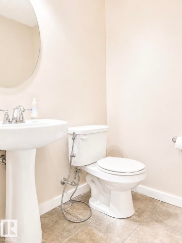 Pedestal sink with chrome fixtures and an oval mirror, complemented by beige wall paint and tile flooring - 5135 1A Avenue Sw, Edmonton, AB - Indoor Photo Showing Bathroom