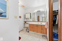 Bathroom featuring a single vanity with wood-finish cabinetry, a large wall-mounted mirror, overhead vanity lighting, and ceramic tile flooring - 