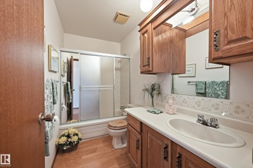 Bathroom featuring wood-finish flooring, a vanity with a solid surface countertop, an integrated sink, and an overhead mirror - 4108 Ramsay Road Nw, Edmonton, AB - Indoor Photo Showing Bathroom
