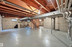Expansive unfinished basement featuring a concrete floor, concrete walls, exposed wood ceiling joists, and a wood-frame staircase - 