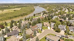 Residential neighborhood featuring a meandering river, mature tree canopy, varied architectural styles, and solar panel installations on select rooftops - 
