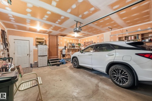 Concrete flooring garage featuring an overhead door track system, an automatic garage door opener, two distinct entry doors, and built-in shelving - 4108 Ramsay Road Nw, Edmonton, AB - Indoor Photo Showing Garage