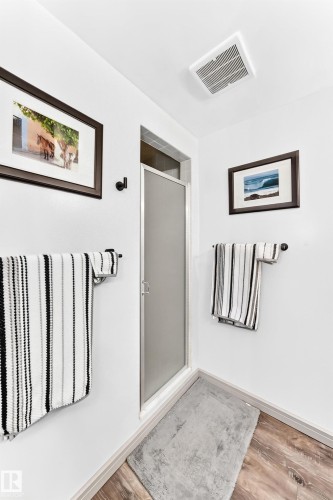 Shower enclosure with frosted glass door, light wood-finish flooring, and crisp white walls - #401 14810 51 Av Nw, Edmonton, AB - Indoor Photo Showing Other Room