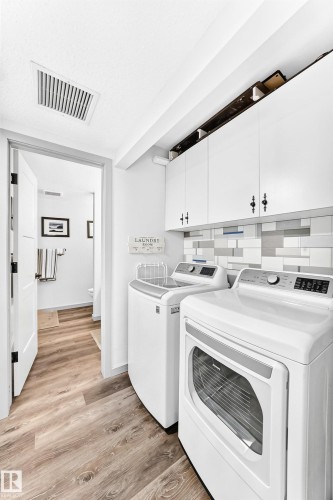 Dedicated laundry area featuring wood-finish flooring, white cabinetry, and a subway tile backsplash - #401 14810 51 Av Nw, Edmonton, AB - Indoor Photo Showing Laundry Room