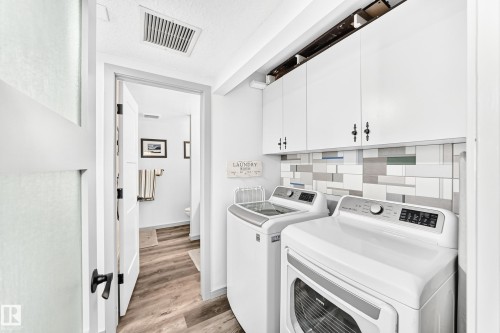 Laundry area featuring white cabinetry, a decorative tiled backsplash, wood-finish flooring, and a white door with black hardware - #401 14810 51 Av Nw, Edmonton, AB - Indoor Photo Showing Laundry Room