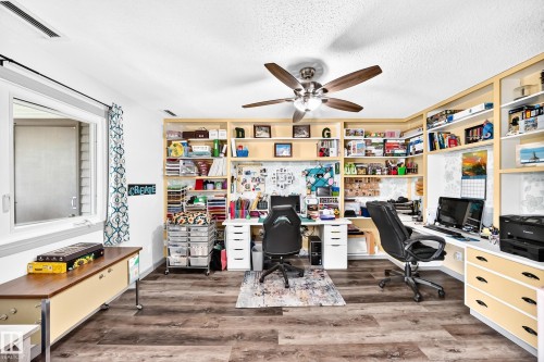 Dedicated workspace featuring extensive built-in shelving, wood-finish flooring, a ceiling fan, and a large window - #401 14810 51 Av Nw, Edmonton, AB - Indoor Photo Showing Office