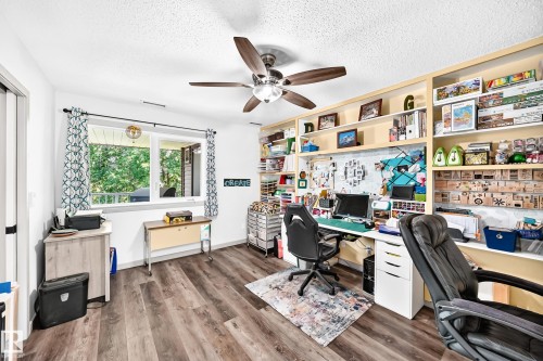 Spacious room featuring wood-finish flooring, a contemporary ceiling fan, and built-in shelving with integrated lighting - #401 14810 51 Av Nw, Edmonton, AB - Indoor Photo Showing Office