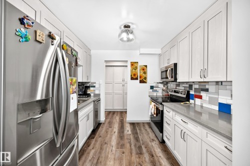 Galley kitchen featuring wood-finish flooring, white shaker-style cabinetry, stainless steel appliances, light gray countertops, and a subway tile backsplash with accent colors - #401 14810 51 Av Nw, Edmonton, AB - Indoor Photo Showing Kitchen With Upgraded Kitchen
