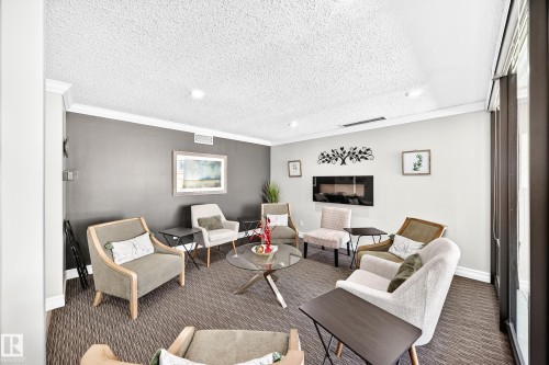 Carpeted gathering space featuring recessed lighting, crown molding, a built-in electric fireplace, and large windows with vertical blinds - #401 14810 51 Av Nw, Edmonton, AB - Indoor Photo Showing Living Room With Fireplace