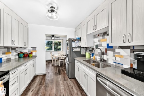 Kitchen featuring light-finish cabinetry, stainless steel appliances, grey countertops, and a multicolor subway tile backsplash - #401 14810 51 Av Nw, Edmonton, AB - Indoor Photo Showing Kitchen With Double Sink