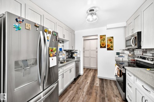 Galley kitchen featuring wood-finish flooring, light-toned cabinetry, and a subway tile backsplash - #401 14810 51 Av Nw, Edmonton, AB - Indoor Photo Showing Kitchen With Double Sink