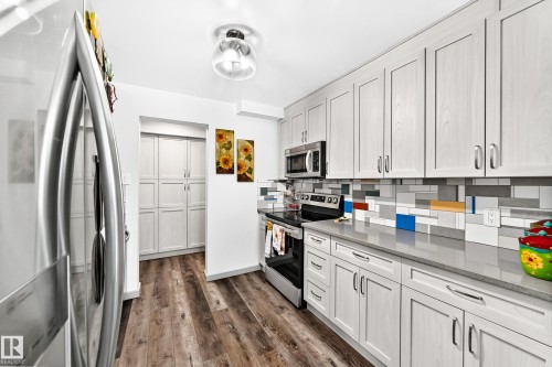 Modern kitchen featuring stainless steel appliances, wood-finish flooring, light-toned cabinetry, solid surface countertops, and a vibrant tile backsplash - #401 14810 51 Av Nw, Edmonton, AB - Indoor Photo Showing Kitchen With Upgraded Kitchen