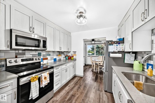 Modern kitchen featuring stainless steel appliances, light-toned cabinetry, a vibrant tile backsplash, durable countertops, and wood-finish flooring - #401 14810 51 Av Nw, Edmonton, AB - Indoor Photo Showing Kitchen With Double Sink With Upgraded Kitchen