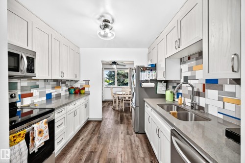 Galley kitchen featuring light wood-finish cabinetry, stainless steel appliances, a double basin sink with a gooseneck faucet, light grey countertops, and wood-finish flooring - #401 14810 51 Av Nw, Edmonton, AB - Indoor Photo Showing Kitchen With Double Sink With Upgraded Kitchen