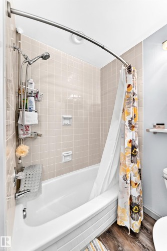 Bathroom featuring a white bathtub, beige square wall tiles, and wood-finish flooring - #401 14810 51 Av Nw, Edmonton, AB - Indoor Photo Showing Bathroom