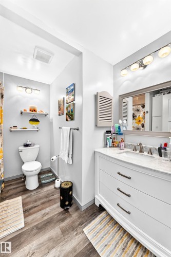 Bathroom featuring a white vanity with integrated sink, a large wall-mounted mirror, and wood-finish flooring - #401 14810 51 Av Nw, Edmonton, AB - Indoor Photo Showing Bathroom