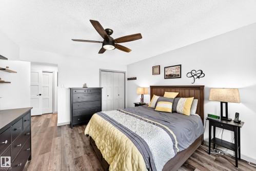 Spacious room featuring wood-finish flooring, a ceiling fan with integrated lighting, and multiple white doors - #401 14810 51 Av Nw, Edmonton, AB - Indoor Photo Showing Bedroom