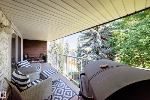 Expansive covered balcony featuring a textured exterior wall, white panel ceiling, and metal railing - #401 14810 51 Av Nw, Edmonton, AB - Outdoor With Deck Patio Veranda With Exterior