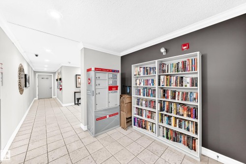 Tiled common area featuring white crown molding and a built-in bookshelf against a dark accent wall - #401 14810 51 Av Nw, Edmonton, AB - Indoor Photo Showing Other Room