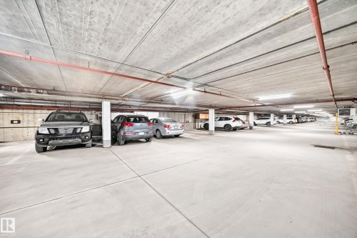 Underground parking garage featuring concrete flooring, concrete walls, concrete ceiling, fluorescent lighting, and visible red piping - #401 14810 51 Av Nw, Edmonton, AB - Indoor Photo Showing Garage