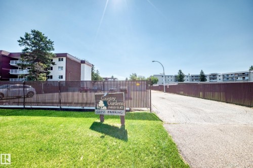 Expansive green lawn with a dedicated guest parking sign and a paved driveway entrance - #401 14810 51 Av Nw, Edmonton, AB - Outdoor