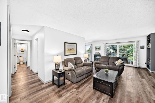 Spacious living area featuring wood-finish flooring, white walls, and a sliding glass door leading to a balcony - #401 14810 51 Av Nw, Edmonton, AB - Indoor Photo Showing Living Room