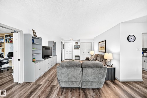 Open-concept living area with wood-finish flooring, white walls, and built-in shelving - #401 14810 51 Av Nw, Edmonton, AB - Indoor Photo Showing Living Room