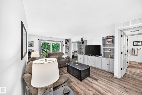 Bright living area featuring wood-finish flooring, a wall of built-in cabinetry, and a sliding glass door opening to an outdoor space - #401 14810 51 Av Nw, Edmonton, AB - Indoor