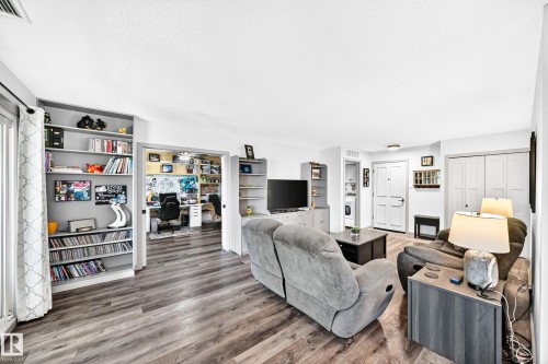 Spacious living area featuring wood-finish flooring, built-in shelving, and light-toned walls - #401 14810 51 Av Nw, Edmonton, AB - Indoor