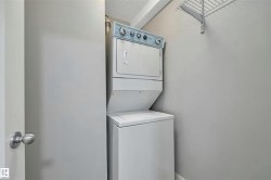 Dedicated laundry area featuring a white stacked washer and dryer unit, complemented by neutral wall tones and a wall-mounted wire shelf - 